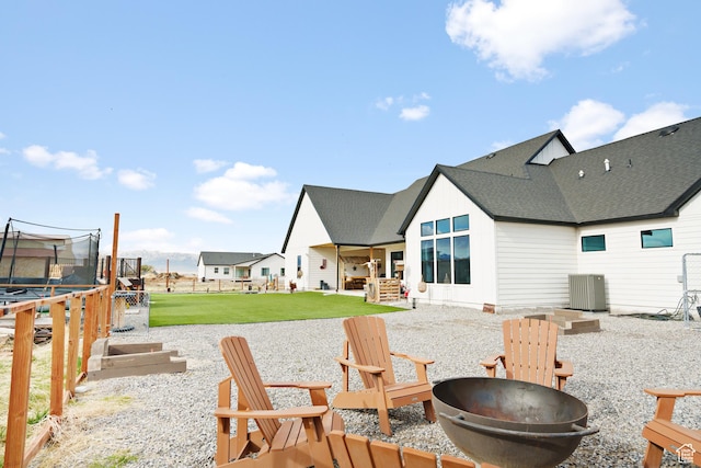 rear view of house with a fire pit, a trampoline, a yard, central AC, and a patio area