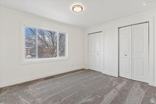 unfurnished bedroom featuring carpet floors, ornamental molding, and two closets