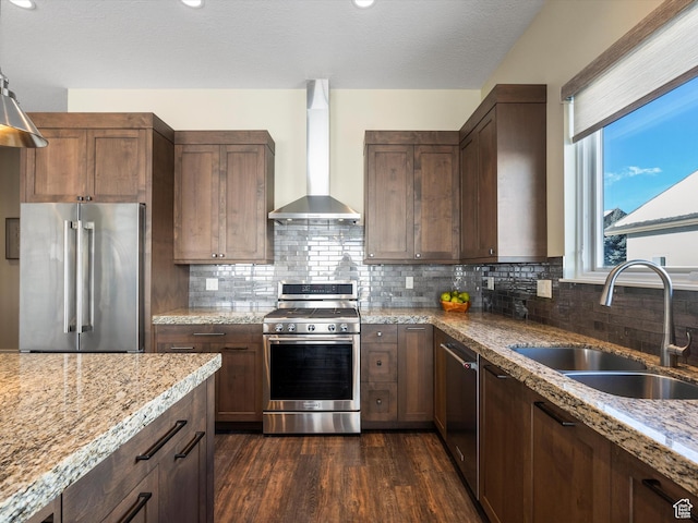 kitchen with dark wood finished floors, a sink, light stone counters, stainless steel appliances, and wall chimney exhaust hood