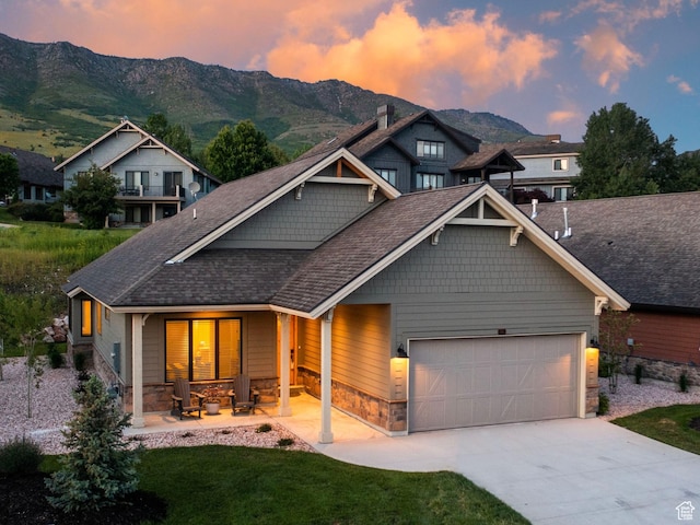 view of front of house featuring a garage, covered porch, stone siding, concrete driveway, and a mountain view
