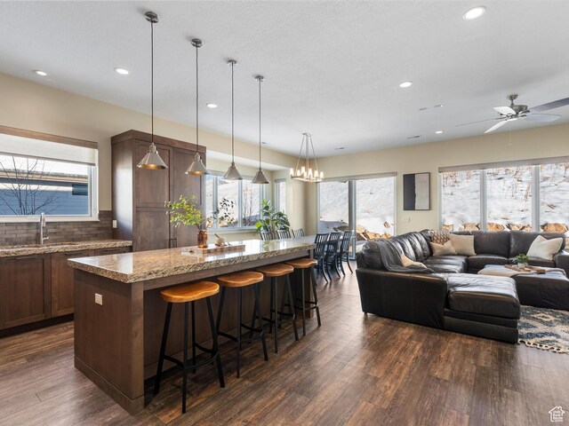 kitchen featuring a kitchen island, open floor plan, recessed lighting, a sink, and dark wood finished floors
