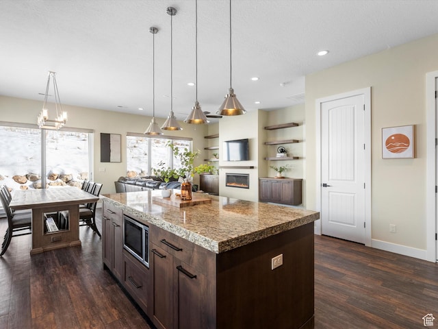 kitchen with stainless steel microwave, dark wood-style floors, dark brown cabinets, and hanging light fixtures