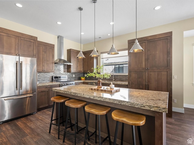 kitchen featuring appliances with stainless steel finishes, decorative backsplash, a breakfast bar, and wall chimney exhaust hood