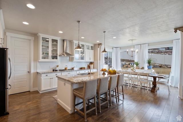 kitchen featuring stainless steel appliances, sink, wall chimney range hood, a center island with sink, and white cabinets