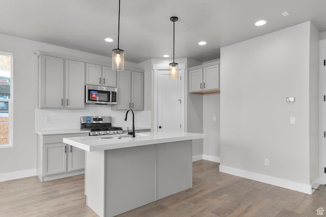 kitchen with a sink, tasteful backsplash, appliances with stainless steel finishes, light wood finished floors, and light countertops