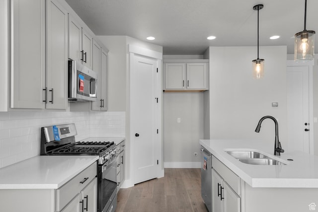 kitchen with pendant lighting, a sink, backsplash, wood finished floors, and stainless steel appliances