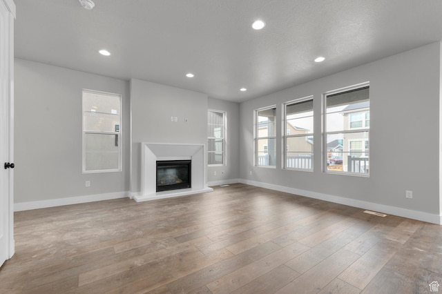 unfurnished living room featuring a glass covered fireplace, recessed lighting, wood finished floors, and baseboards