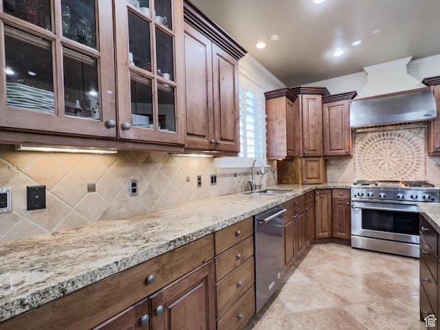 kitchen with sink, ornamental molding, light stone counters, custom range hood, and appliances with stainless steel finishes