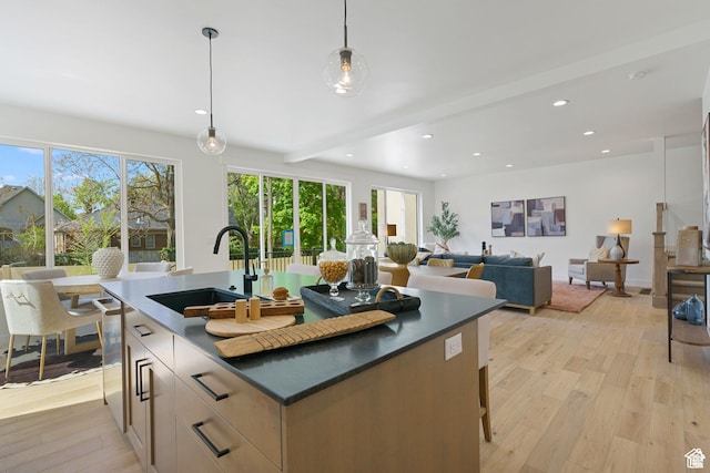 kitchen with sink, beamed ceiling, an island with sink, light hardwood / wood-style floors, and decorative light fixtures
