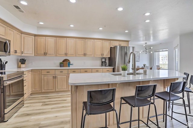 kitchen featuring a kitchen island with sink, sink, light hardwood / wood-style floors, stainless steel appliances, and a chandelier
