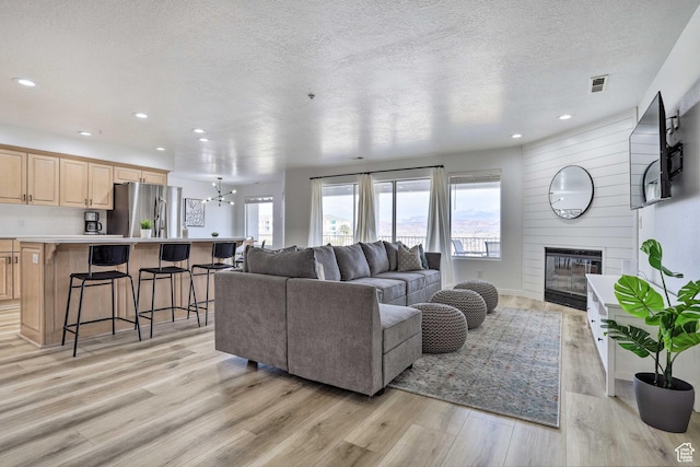 living room featuring a fireplace, light wood-type flooring, a textured ceiling, and a chandelier