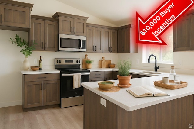 kitchen featuring appliances with stainless steel finishes, a sink, vaulted ceiling, light countertops, and light wood-style floors