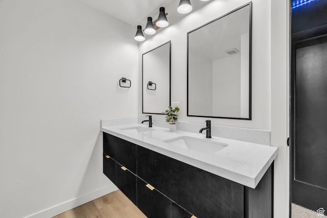 full bath featuring double vanity, wood finished floors, baseboards, and a sink
