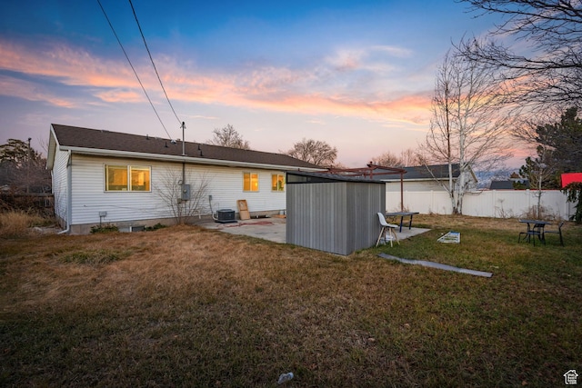 back house at dusk featuring a lawn, central AC unit, and a storage shed