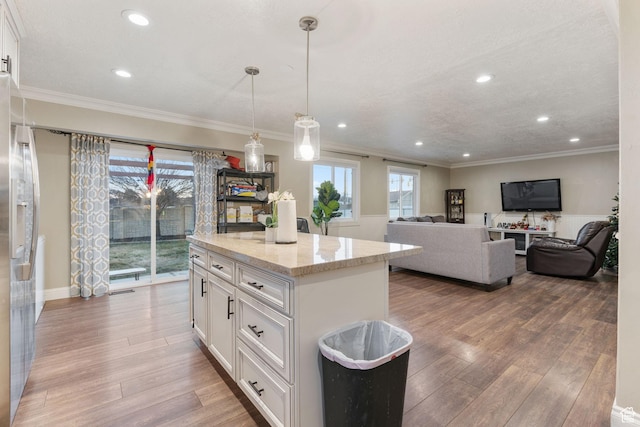 kitchen with a kitchen island, light stone counters, white cabinetry, and hanging light fixtures