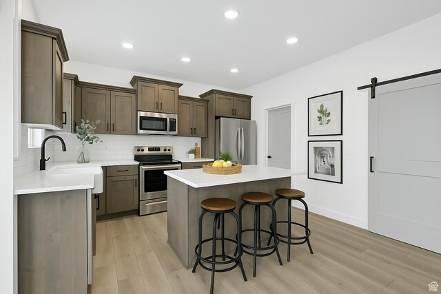1317 N 1850 W, Clinton, UT 84015 - kitchen featuring appliances with stainless steel finishes, a kitchen bar, decorative backsplash, a kitchen island, and light wood-type flooring