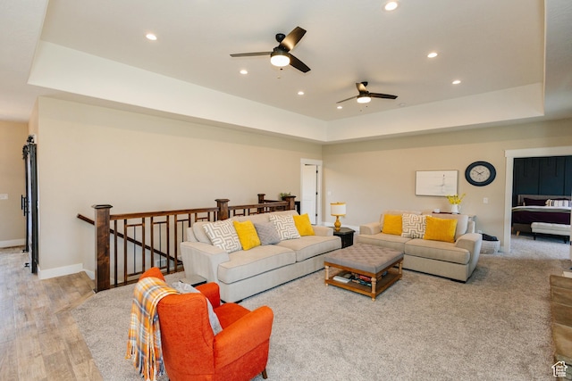 living room with light hardwood / wood-style floors, a raised ceiling, and ceiling fan