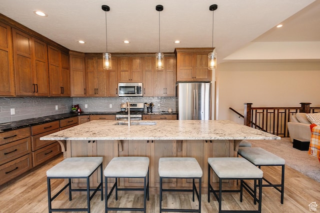 kitchen with hanging light fixtures, dark stone countertops, an island with sink, a kitchen bar, and stainless steel appliances