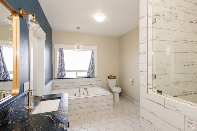 bathroom with tiled tub, vanity, a notable chandelier, and toilet