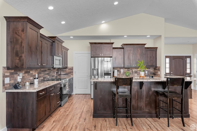 kitchen with lofted ceiling, a center island with sink, a kitchen breakfast bar, decorative backsplash, and stainless steel appliances
