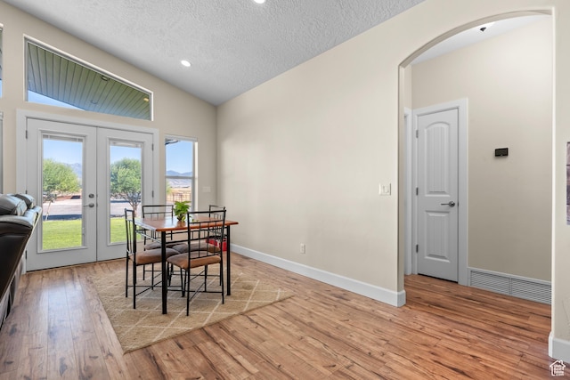 dining area with french doors, a textured ceiling, light hardwood / wood-style floors, and vaulted ceiling