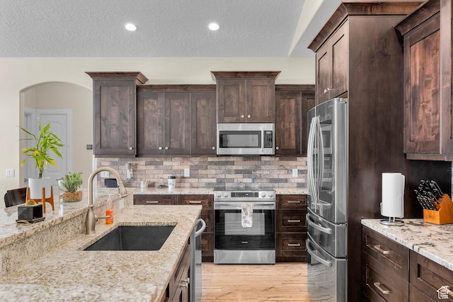 kitchen featuring sink, stainless steel appliances, light stone counters, backsplash, and dark brown cabinets