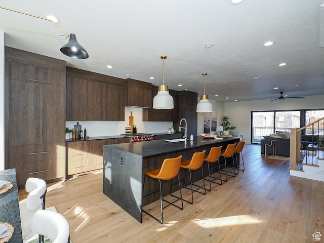 kitchen featuring modern cabinets, a sink, light wood-type flooring, dark countertops, and a breakfast bar