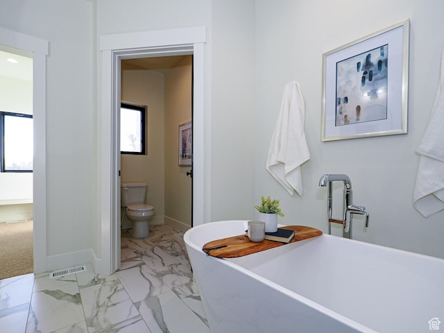 bathroom with visible vents, baseboards, a freestanding tub, toilet, and marble finish floor