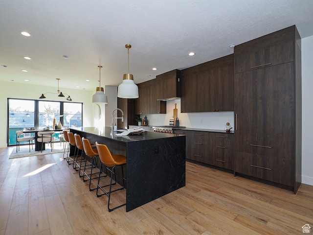 kitchen with a kitchen island with sink, recessed lighting, light wood-type flooring, and a kitchen bar