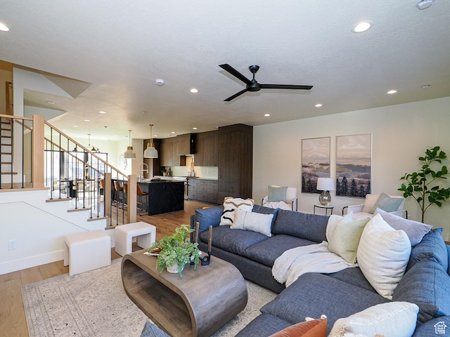 living area with a ceiling fan, recessed lighting, stairs, light wood finished floors, and baseboards