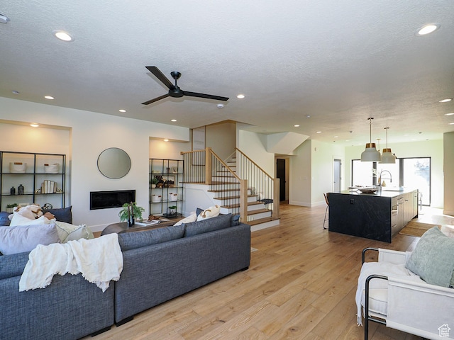 living area with light wood-style flooring, recessed lighting, a ceiling fan, and stairway