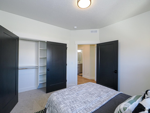 bedroom with visible vents, baseboards, a closet, a textured ceiling, and light carpet