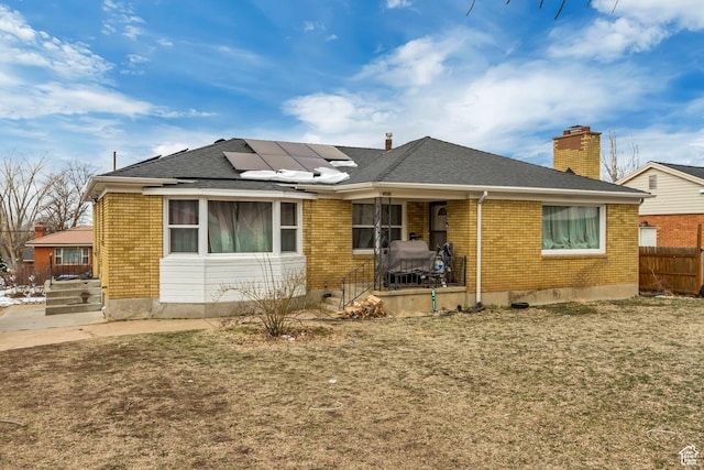 view of front of property featuring roof with shingles, a chimney, fence, brick siding, and roof mounted solar panels