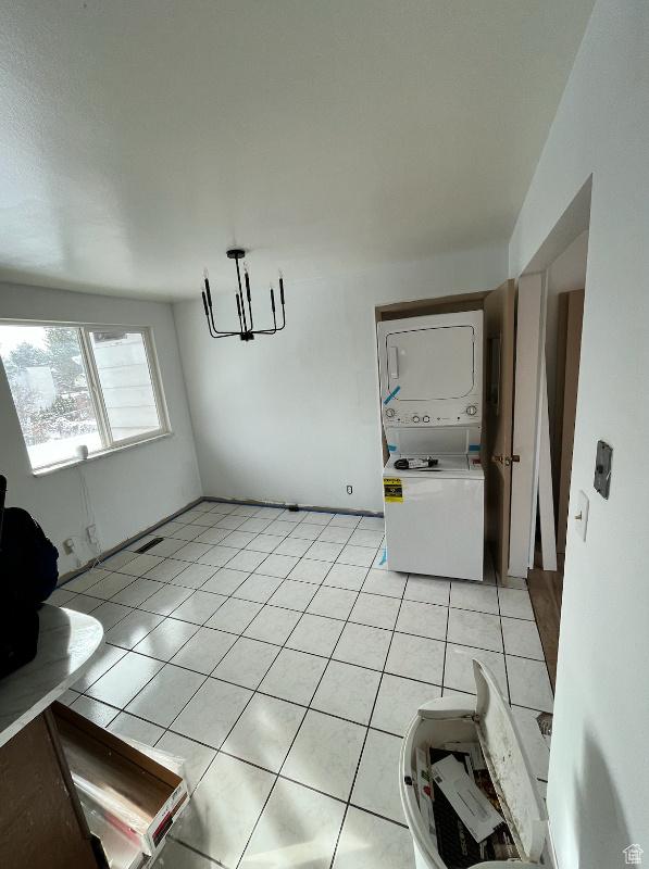 unfurnished dining area featuring light tile patterned flooring, stacked washing maching and dryer, and an inviting chandelier