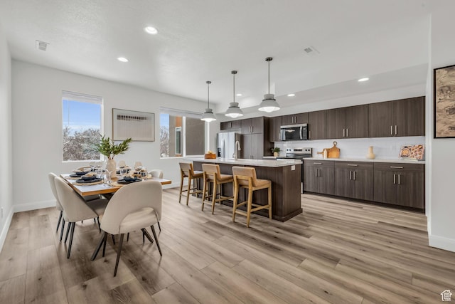 233 E Burch Creek Pl S, Ogden, UT 84405 - kitchen featuring a center island with sink, dark brown cabinetry, light countertops, light wood-style floors, and appliances with stainless steel finishes
