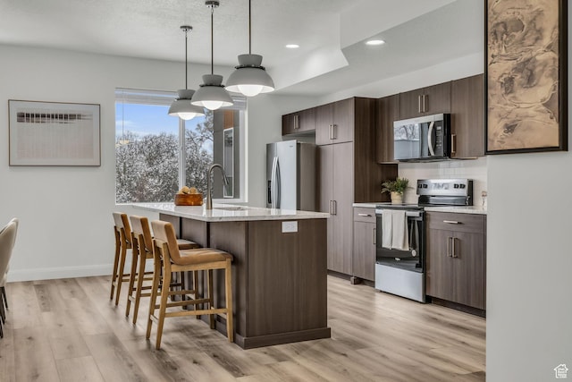 233 E Burch Creek Pl S, Ogden, UT 84405 - kitchen featuring light wood finished floors, dark brown cabinetry, a breakfast bar, appliances with stainless steel finishes, and a sink