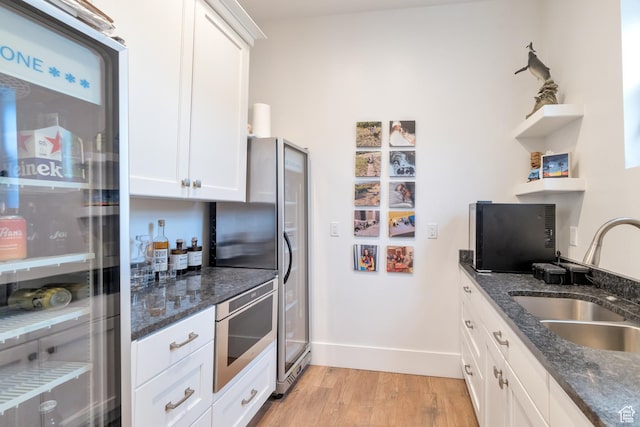 kitchen featuring open shelves, a sink, freestanding refrigerator, white cabinetry, and light wood finished floors
