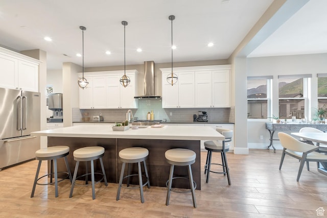 kitchen featuring tasteful backsplash, stainless steel fridge, wall chimney exhaust hood, and a center island with sink