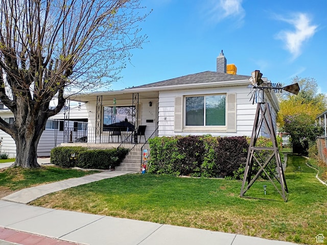 bungalow featuring covered porch, a chimney, and a front lawn