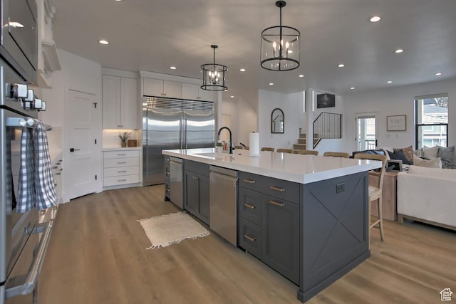 585 N Amber Ln, Garden City, UT 84028 - kitchen featuring stainless steel appliances, decorative light fixtures, a center island with sink, light hardwood / wood-style flooring, and white cabinetry