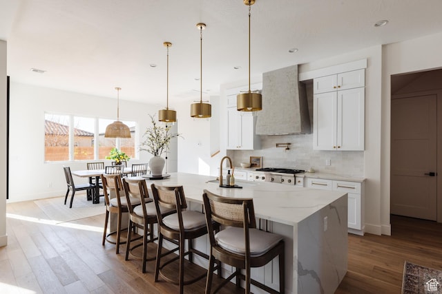 3305 W 2610 S, Hurricane, UT 84737 - kitchen featuring wood finished floors, wall chimney exhaust hood, a kitchen island with sink, white cabinetry, and backsplash