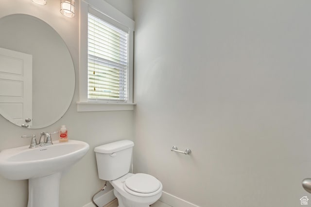 half bathroom with toilet, baseboards, and a sink