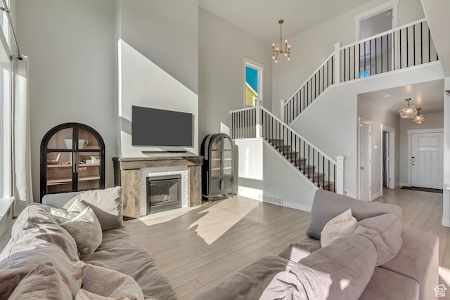 living area with a towering ceiling, a fireplace with flush hearth, wood finished floors, an inviting chandelier, and stairs