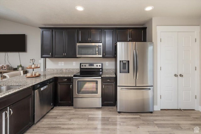kitchen featuring stainless steel appliances, light stone counters, light hardwood / wood-style floors, and sink