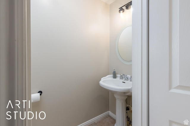 half bath with baseboards, tile patterned flooring, and a sink