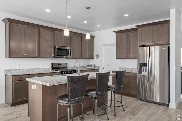 kitchen with dark brown cabinetry, a breakfast bar, light wood finished floors, a kitchen island with sink, and stainless steel appliances