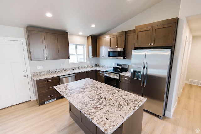 kitchen with light stone counters, dark brown cabinetry, stainless steel appliances, light wood-style flooring, and visible vents
