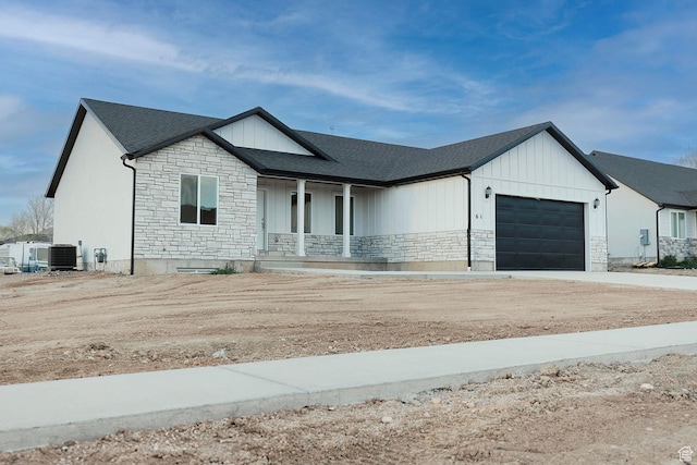 view of front of home featuring stone siding, an attached garage, a porch, and cooling unit