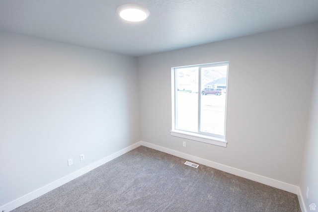 spare room featuring dark colored carpet, visible vents, and baseboards