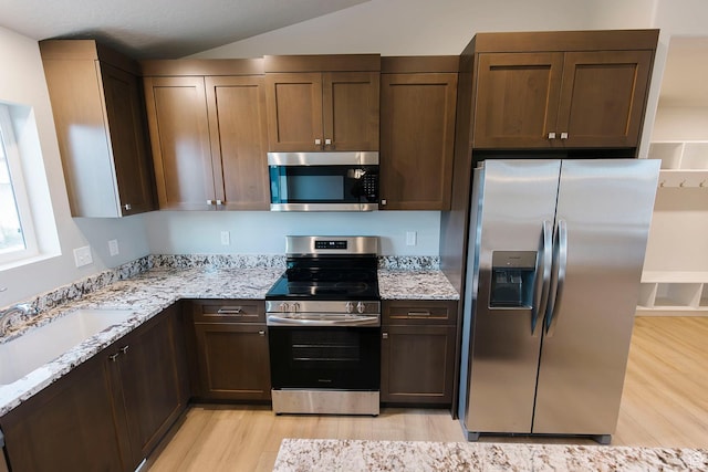 kitchen featuring appliances with stainless steel finishes, light stone countertops, light wood-style floors, and a sink